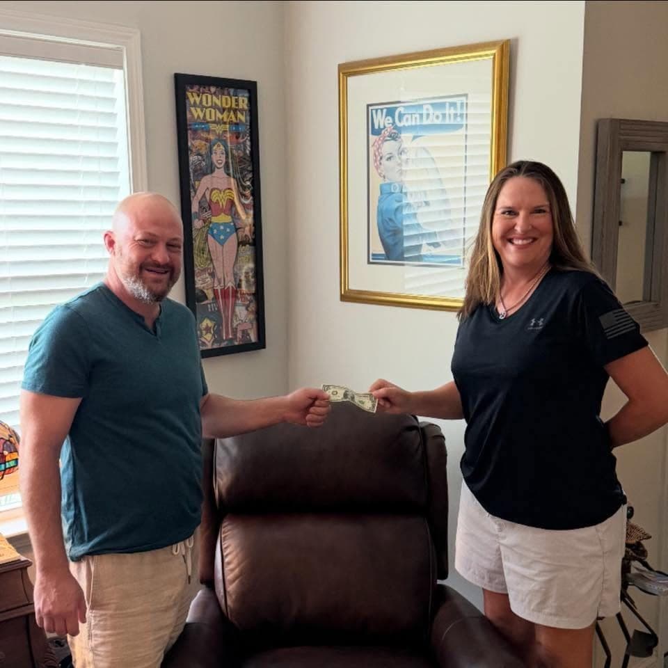 Kent accepting the keys to Seneca Furniture Showcase with a symbolic one-dollar handoff over a leather recliner